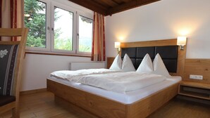 Una cama de madera con ropa de cama blanca, dos lámparas de noche y un ventanal con cortinas.