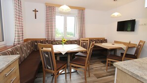 Un comedor con un banco y mesa de madera, una cruz en la pared y un televisor montado sobre la mesa.