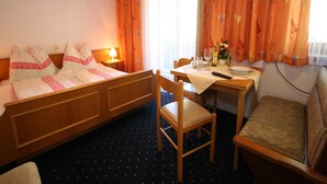A hotel room with a bed, a desk with a chair, a table with a chair, and a window with curtains.