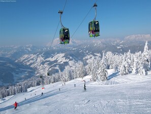 Een skilift met cabines, hangend aan kabels, een besneeuwd berglandschap en skiërs in de verte.