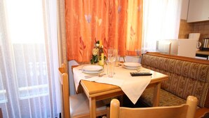 A dining area with a table set for two, a sofa, and a kitchen in the background.