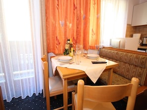 Un comedor con una mesa lista para dos personas, un sofá y una cocina al fondo.