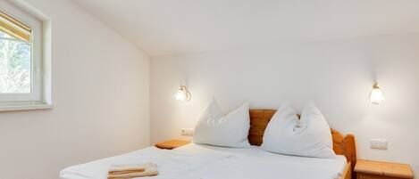 A bedroom with a wooden bed, white bedding, two bedside lamps, a nightstand, and a skylight.