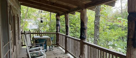 A wooden porch with rocking chairs and a table, surrounded by trees.