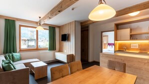 A modern living room with a wooden dining table, sofa, and chairs. A TV is mounted on the wall, and there is a kitchen area with a sink and countertop. - Apartment in Wald near Zillertal Arena (Wald im Pinzgau)
