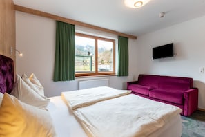 A bedroom with a bed, a purple sofa, a TV, and a window with curtains.