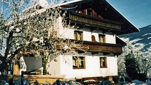Un chalet à deux étages, doté d’un toit en pente, de balcons en bois et surplombant un paysage enneigé.