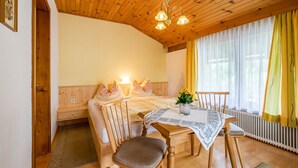 Une pièce chaleureuse avec un plafond en bois, un lit avec des oreillers, une table ornée d’un vase de fleurs et une fenêtre avec des rideaux.
