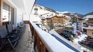 Un balcón con vistas a un pueblo cubierto de nieve, edificios de madera y coches aparcados.