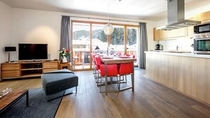 Una sala de estar moderna con un televisor de pantalla plana, un comedor con sillas rojas y una cocina con electrodomésticos de acero inoxidable.