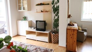 Un salon avec un téléviseur, un meuble, une plante et un canapé.