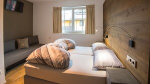 A modern bedroom with a sofa bed, a flat-screen TV mounted on the wall, a window with curtains, and a wooden accent wall. - Modern apartment near the ski area (Brixen im Thale)