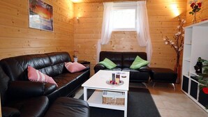 A cozy room with wooden walls, a black leather sofa, a white coffee table, and a small side table with a vase of flowers. - Chalet in Ötztal near Ötz-Hochötz Ski Resort (Umhausen)