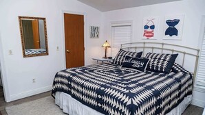 A bedroom with a bed, a mirror, a door, a lamp, and wall art.