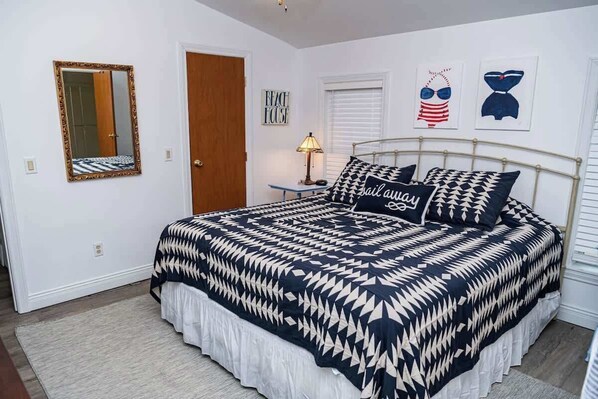 A bedroom with a bed, a mirror, a door, a lamp, and wall art.