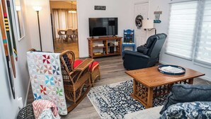 A living room with a television, a blue armchair, a wooden coffee table, and a patterned rug.