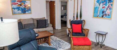 Una sala de estar con un sofá, una butaca, una mesa de centro y dos cuadros en la pared.