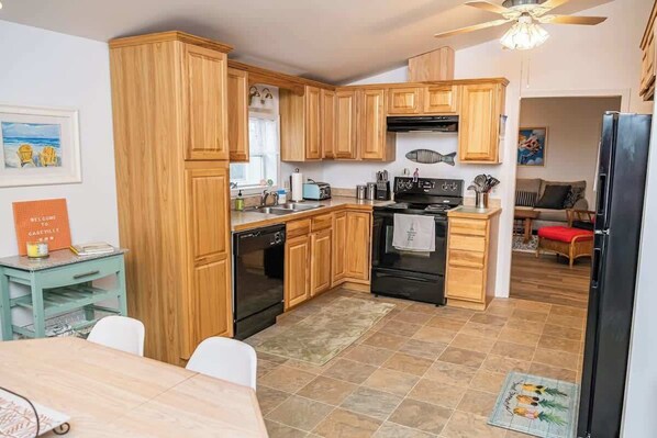 A compact kitchen with wooden cabinets, a black refrigerator, and a dining area with a table and chairs.