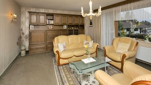 A living room with a sofa set, a glass coffee table, and a chandelier. There are bookshelves and a window with a view. - Apartment in Hinterbichl near Ski Bus (Wängle)