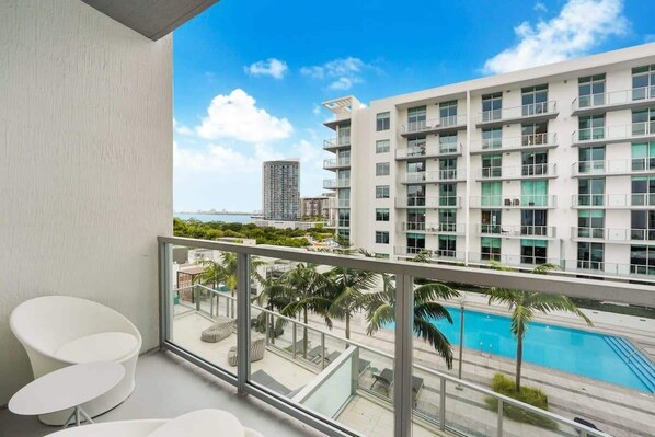 Un balcon avec vue sur un immeuble moderne, une piscine et des palmiers.