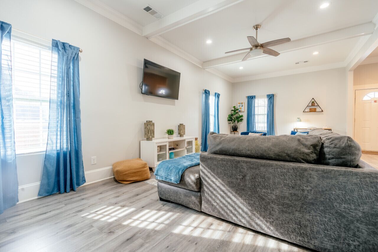 A modern living room with a grey sofa, a flat-screen TV mounted on the wall, and a ceiling fan.