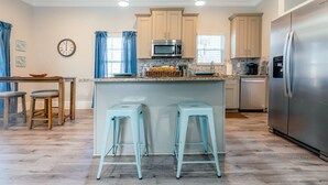 Una cocina moderna con una isla central, dos taburetes de bar, un refrigerador de acero inoxidable y muebles de cocina en tonos claros.