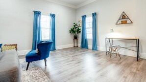 Una habitación amplia con suelo de madera, una silla azul, una mesita y una planta en maceta.