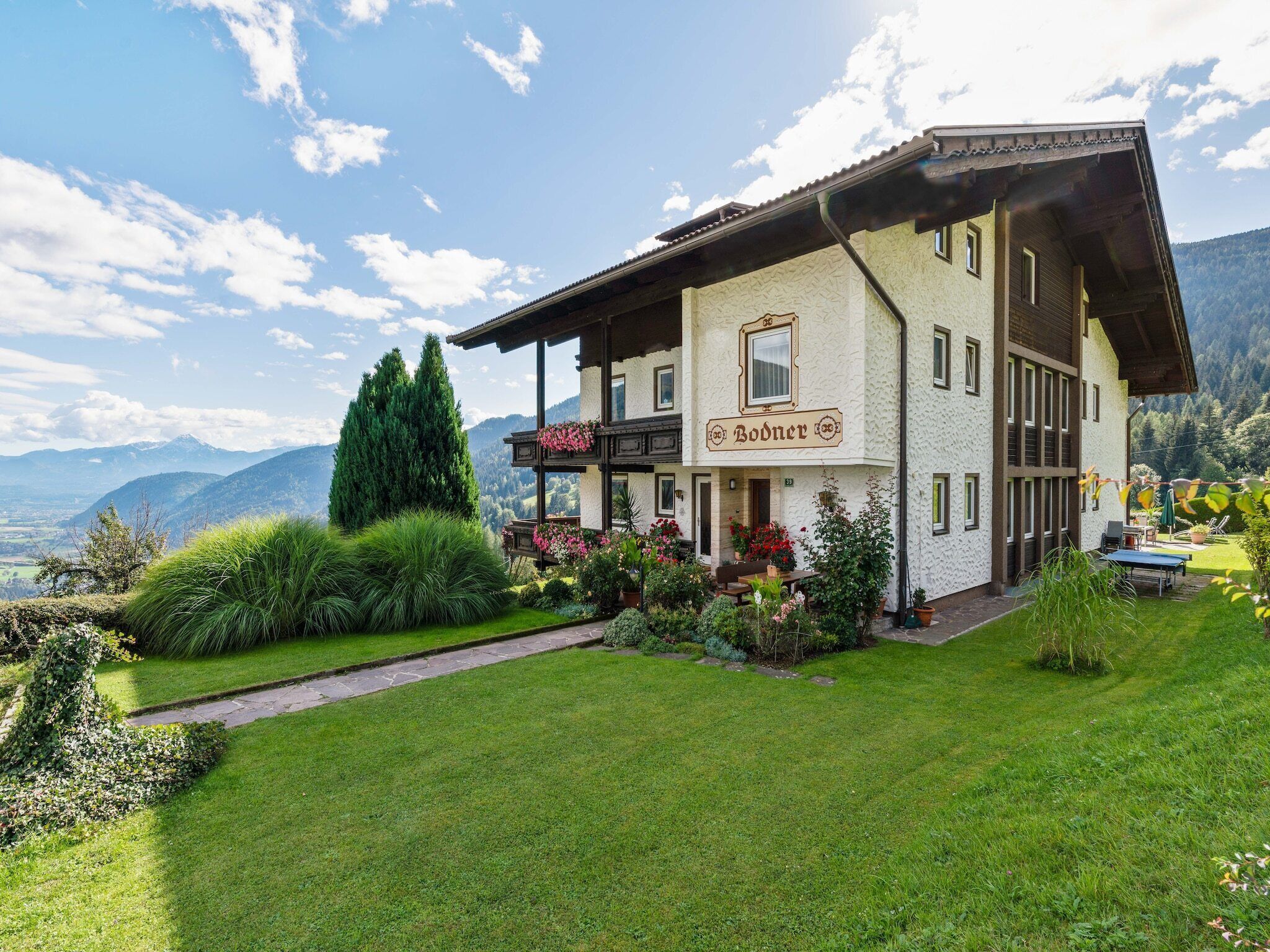 Un bâtiment de style alpin traditionnel, doté d’un balcon, entouré de jardins bien entretenus et offrant une vue sur les montagnes.