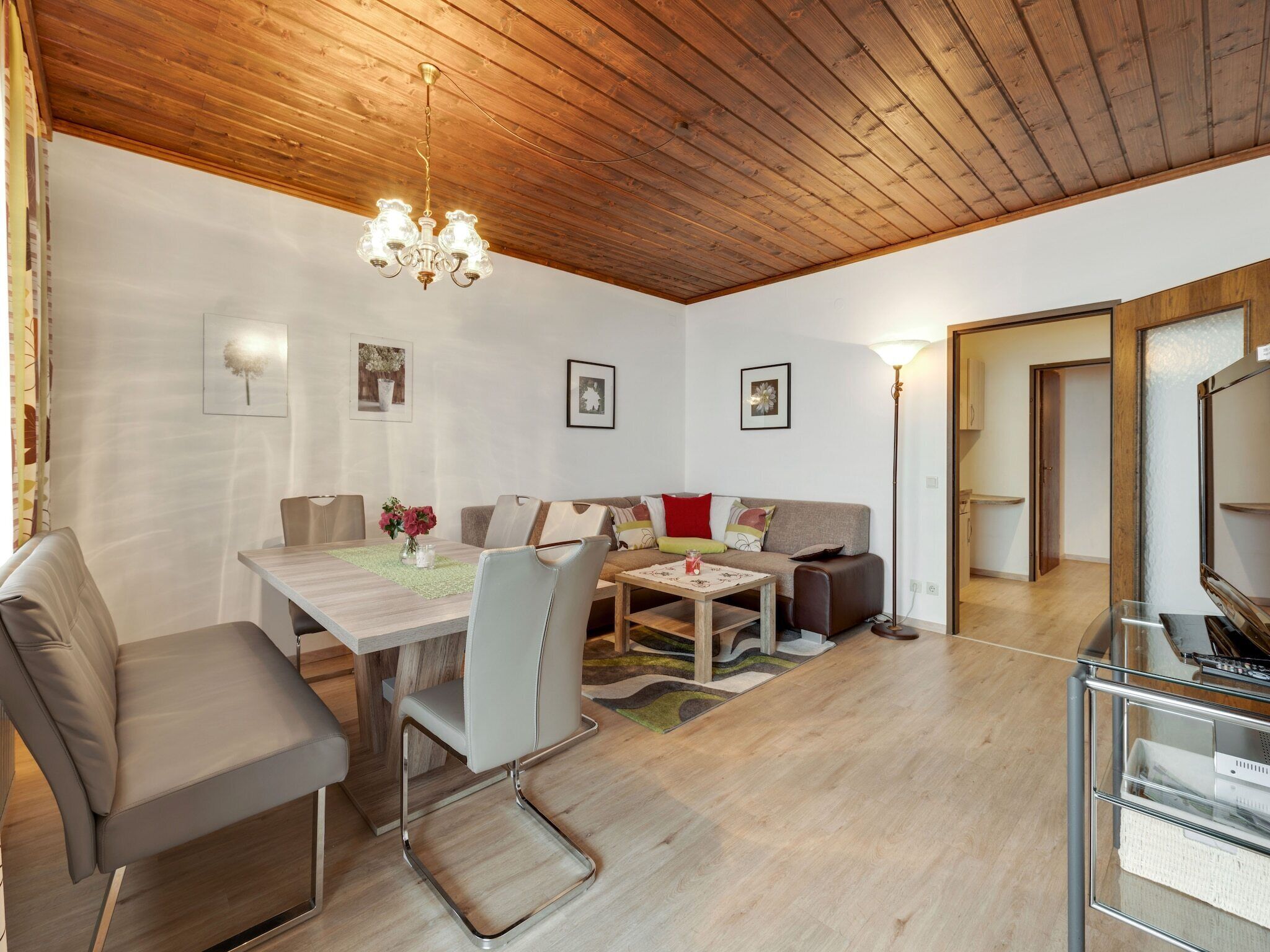 Un salon moderne avec un plafond en bois, une table à manger avec des chaises, un canapé avec des coussins et un lampadaire.