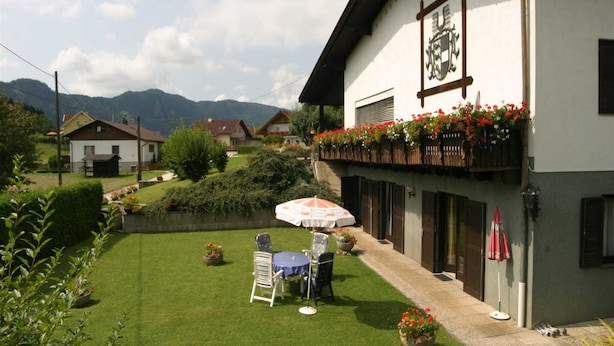 A building with a balcony adorned with flowers, a small outdoor seating area with a table and chairs, and a well-maintained lawn.