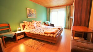 A bedroom with a wooden bed, a bedside table, a chair, and a window with curtains.