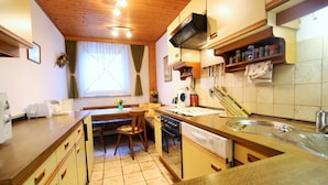 A compact kitchen with wooden cabinets, a dining table with chairs, a built-in oven, and a sink.