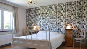 Una camera da letto con un letto in ferro bianco, carta da parati a motivi floreali, un armadietto in legno e una sedia.