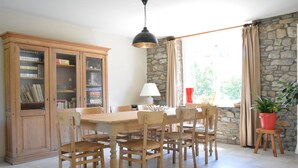 Zona pranzo con tavolo e sedie in legno, un mobile contenente libri, una lampada e una pianta in vaso.