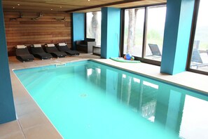 En inomhuspool med solstolar och utsikt över omgivningarna.