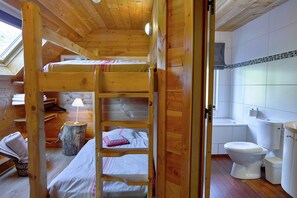 En stuga byggd av trä med en våningssäng, ett litet bord med en lampa, en stol och ett badrum med toalett och handfat.