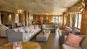A cozy log cabin interior with wicker furniture, stone walls, and a dining area. - Luxurious Holiday Home in Stoumont with Pool & Bar (Stoumont)