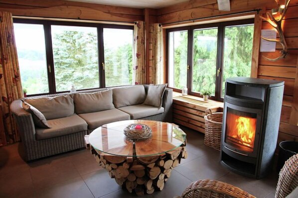 En mysig stuga med en soffa, ett bord med glasskiva och vedstaplar, och en vedeldad kamin.
