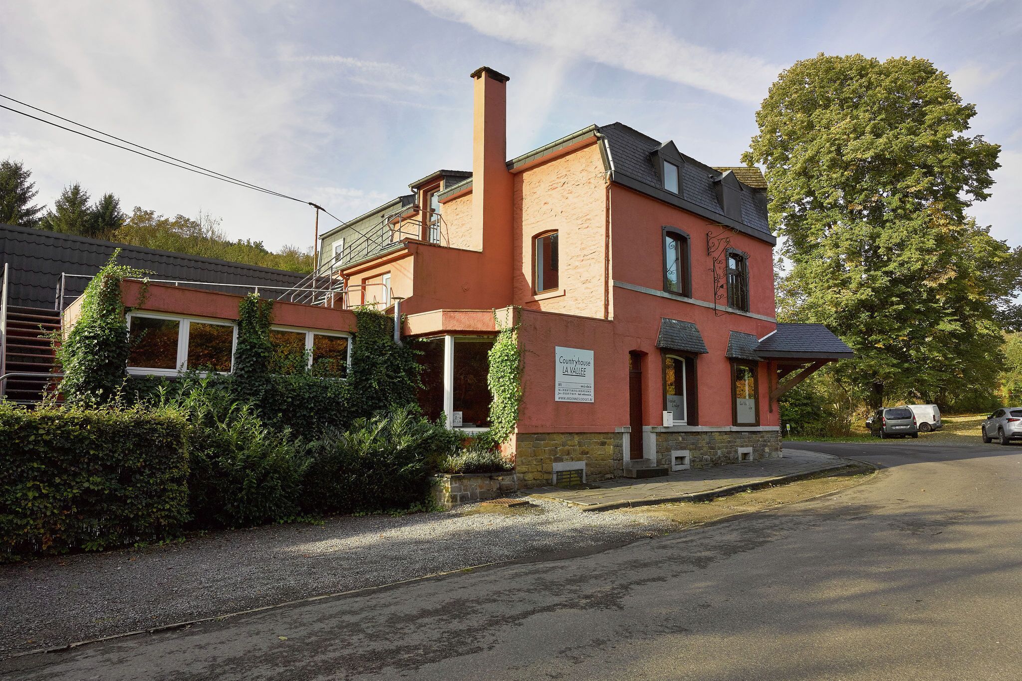 A red building with a chimney, a sign reading "Countryhouse La Vallee," and a parking area with cars.