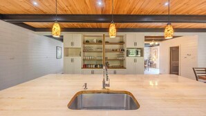 Een keuken met een centraal eiland, houten plafond, hanglampen en inbouwkeuken.