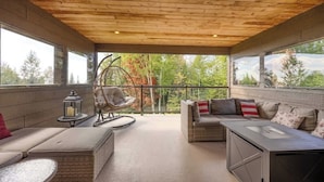 Een overdekt terras met houten plafond, rieten meubels en uitzicht op bomen.