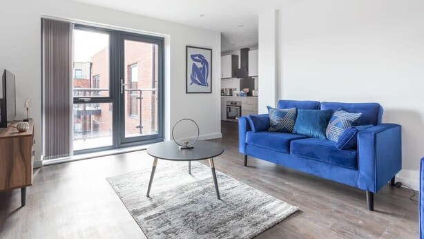 Un salón moderno con un sofá azul, una mesa de centro redonda y un ventanal con vistas a la ciudad.