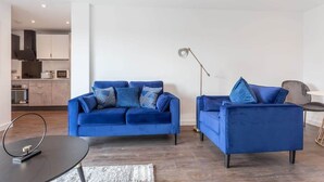 Una sala de estar moderna con un sofá azul, una pequeña mesa redonda y una lámpara de pie.