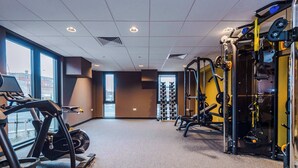 Un gimnasio con equipamiento cardiovascular, máquinas de pesas y un estante con mancuernas.