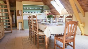 A dining area with a high ceiling and skylight, wooden chairs and a table set for a meal, and a kitchen in the background. - Spacious, atmospheric upper floor of a farmhouse with garden (Loenhout)