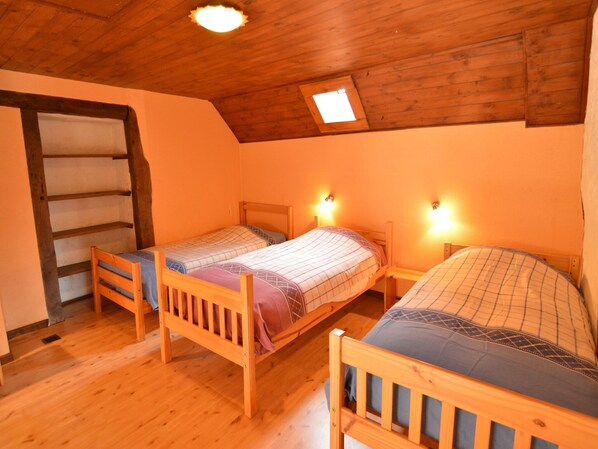 A small, cozy room with two wooden beds, a wooden ladder, and a sloped ceiling with a skylight.