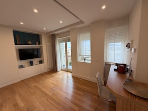 Una cocina moderna con suelo de madera, electrodomésticos integrados y una puerta corredera de vidrio que da a un balcón.