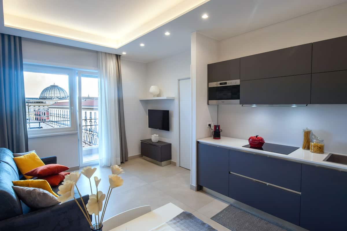A modern living room with a sofa, a flat-screen TV, and a view of a cityscape through large windows.
