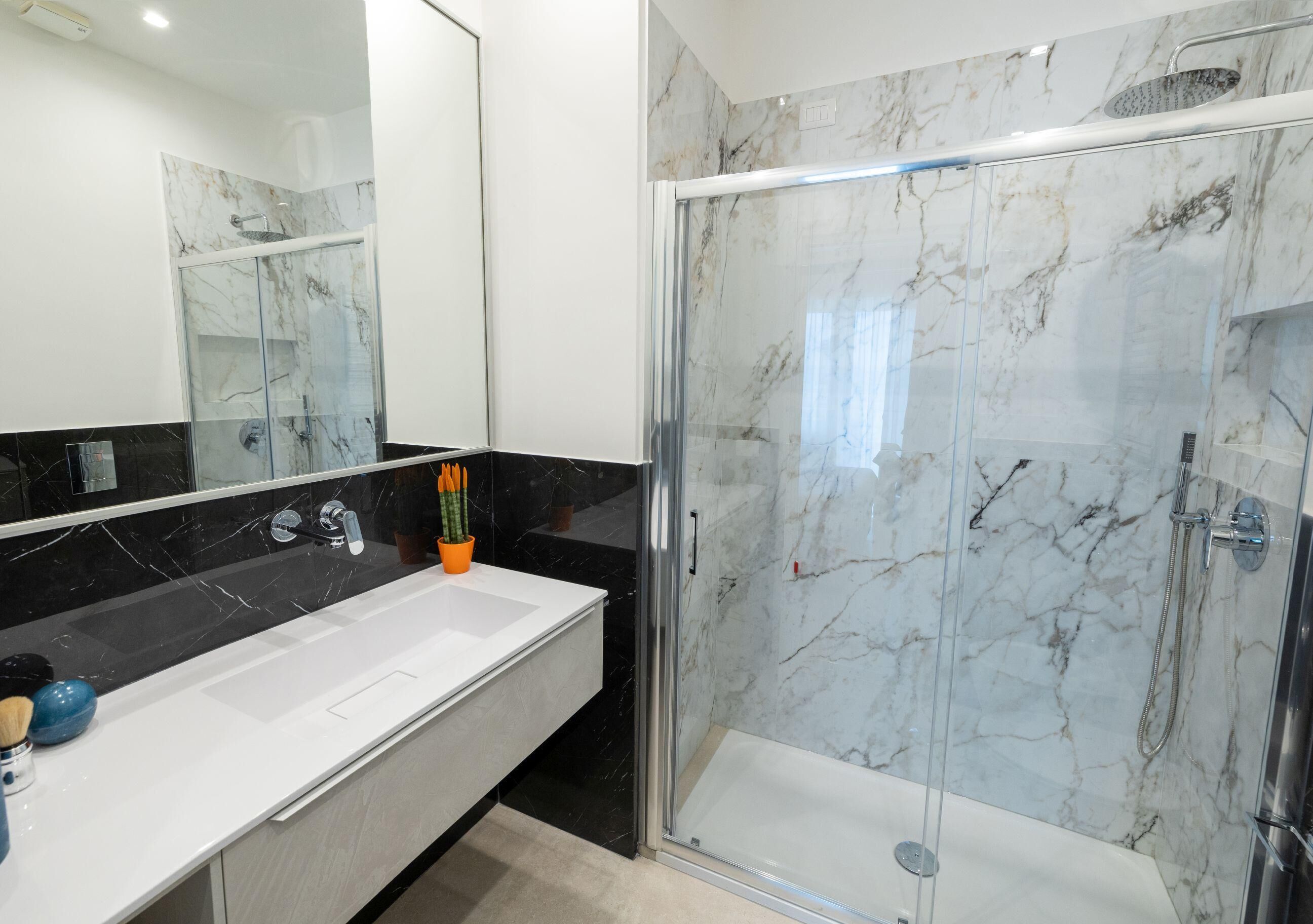 Une salle de bain moderne avec une douche à parois de verre, un lavabo blanc et un pare-baignoire en marbre.