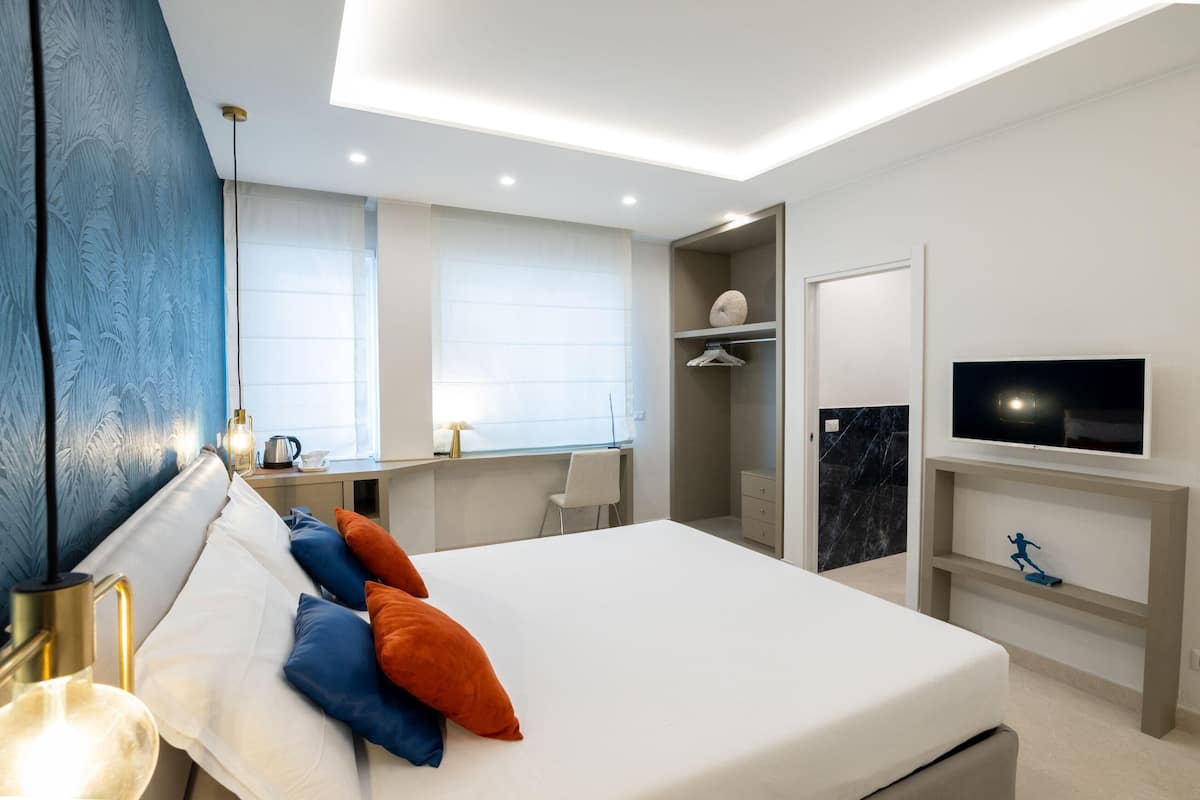 A modern hotel room with a large bed, a desk, a TV, and a wardrobe.